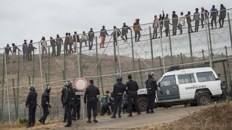 مهاجرون أفارقة يتسلقون السياج الحديدي بحضور الشرطة الإسبانية بمدينة مليلة، 17 مايو/آذار 2014   