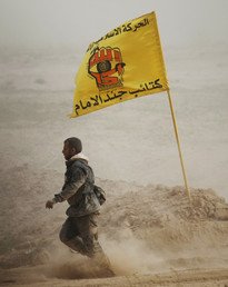 مقاتل يسير بالقرب من علم المقاتلين الشيعة الذي كتب عليه "كتائب جند الإمام"، 12 مارس 2015 