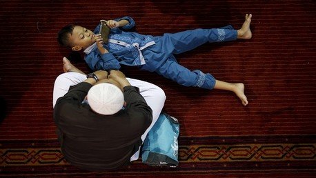 طفل يلعب بهاتف أبيه قبل صلاة الجمعة بمسجد الاستقلال خلال شهر رمضان المبارك في جاكرتا الإندونيسية