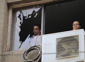 سكان المنطقة المحيطة بالانفجار يشاهدون الموقع من نافذة منزلهم المحطمة بفعل الإنفجار 29 يونيو 2015