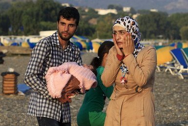 اللاجئ السوري محمد يحمل طفلته البالغة من العمر شهرين، وبجانبه زوجته كوثر، بعد وصولهما شاطئ جزيرة كوس اليونانية، 9 أغسطس 2015  