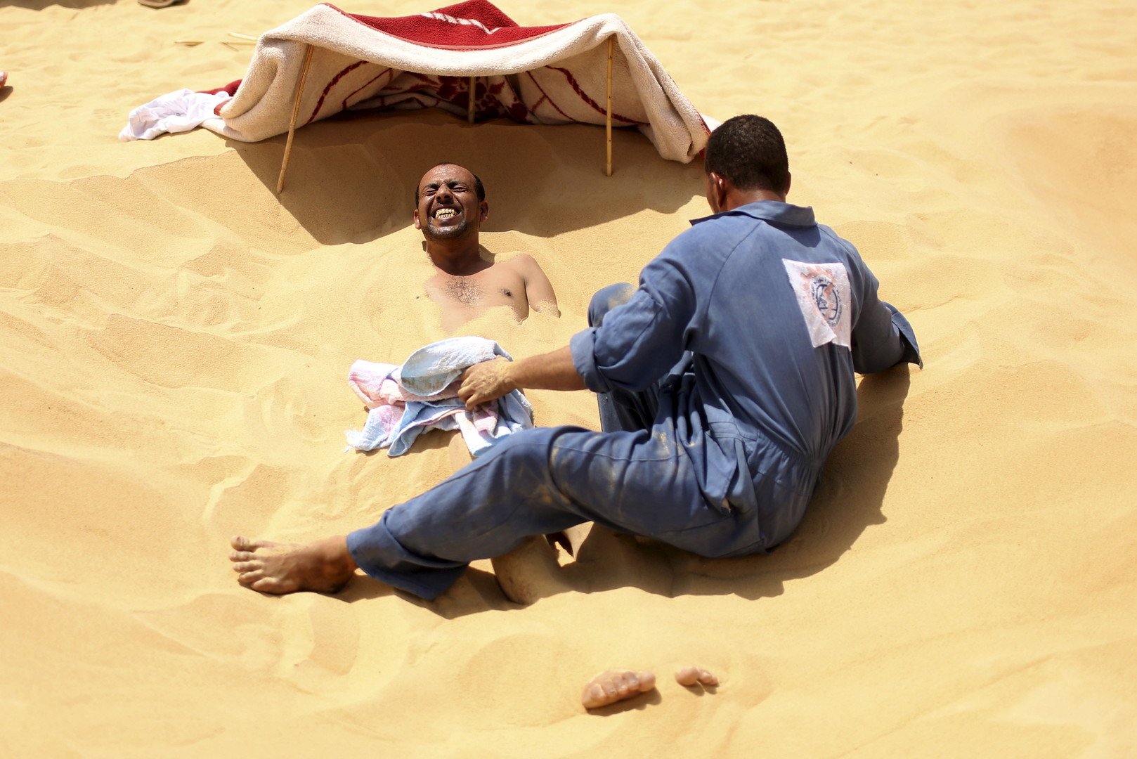معالج يقوم بتغطية أحد المستجمين بالرمال الساخنة في سيوة، مصر، 11 أغسطس 2015