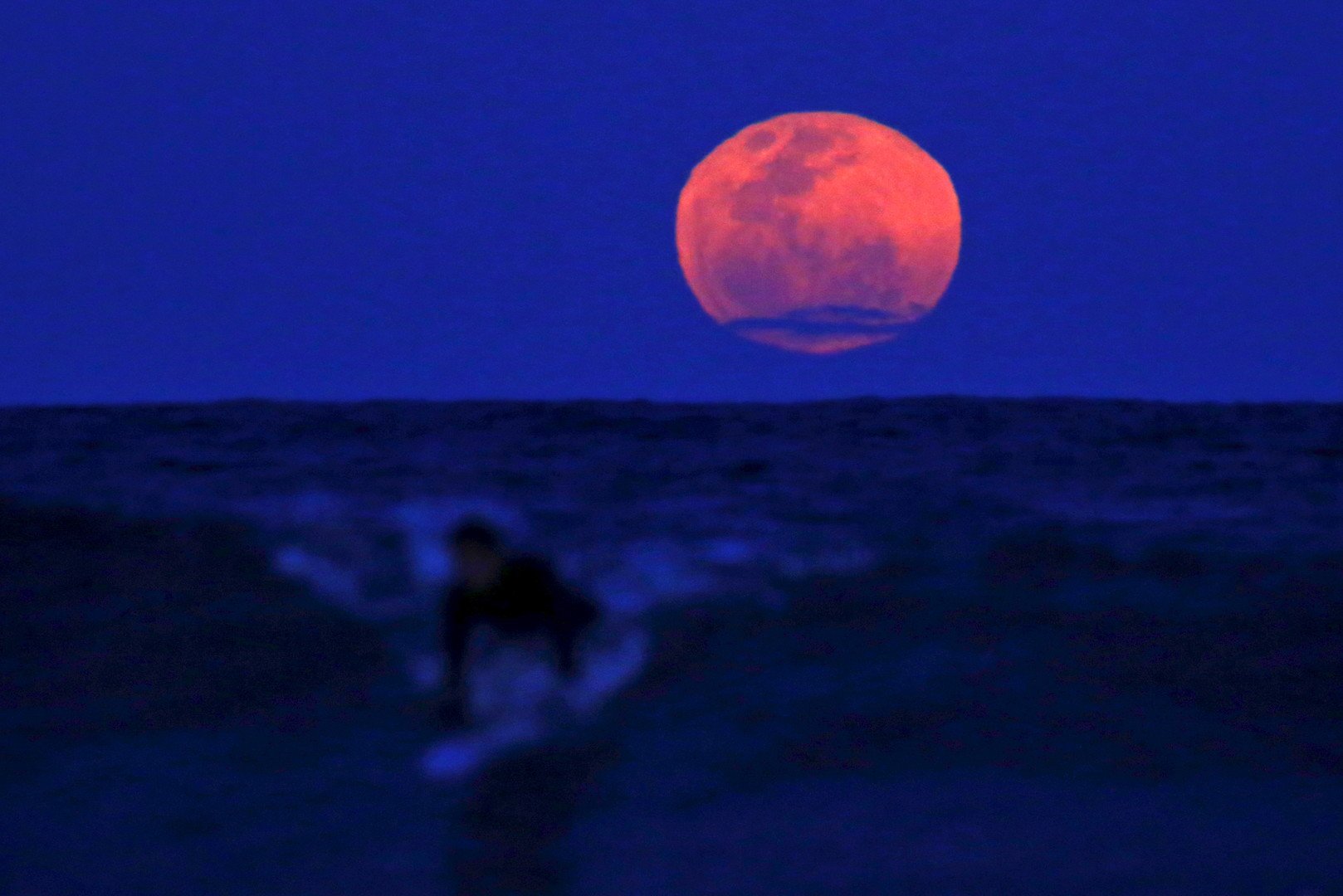 مشهد لأحد راكبي الأمواج وخلفه صورة بديعة لخسوف القمر العملاق على أحد شواطئ سيدني في أستراليا، 28 سبتمبر/أيلول 2015 