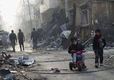 طفل يركب دراجة هوائية صغيرة في شارع أبنيته مهدمة في منطقة محاصرة في حمص