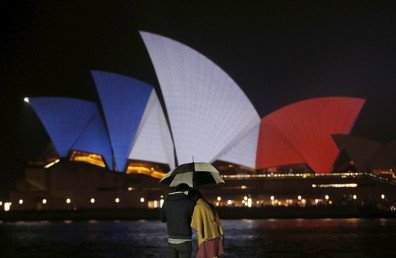 اثنان يقفان تحت المطر على خلفية مبنى الأوبرا المضاء بألوان العلم الفرنسي في سيدني-أستراليا