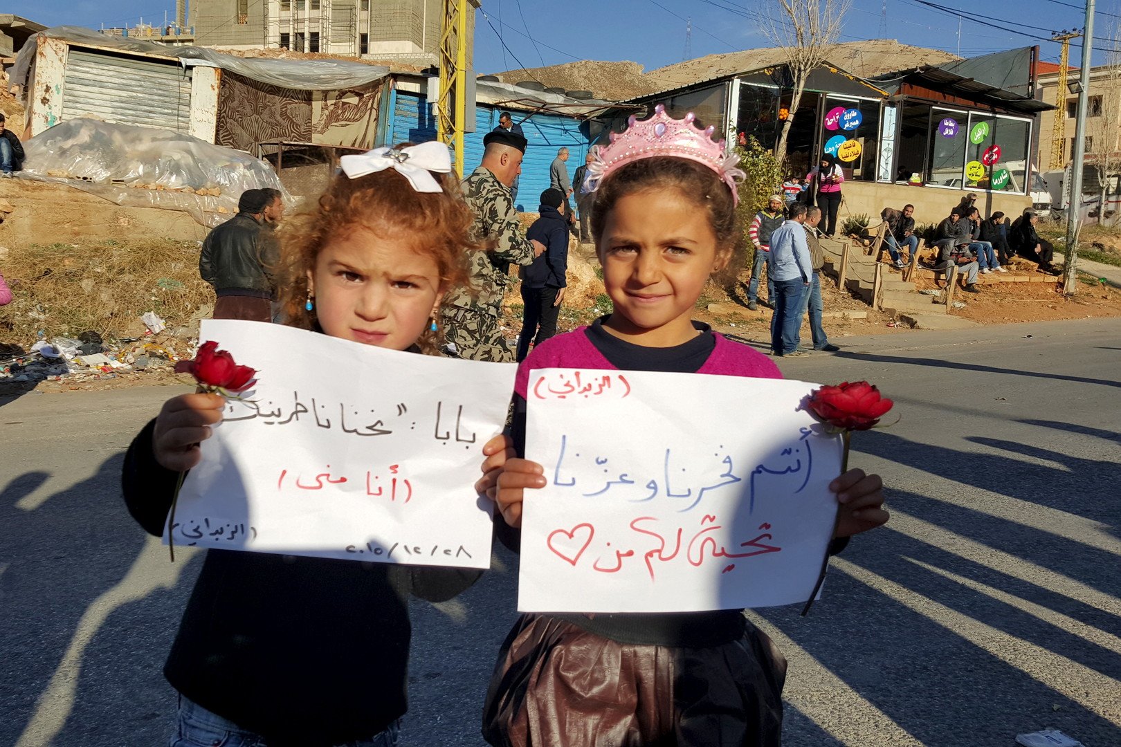 فتيات يحملن لافتات أثناء انتظارهن عند المعبر الحدودي بين لبنان وسوريا لوصول أقاربهن من المقاتلين المتمردين الذين غادروا بلدة الزبداني، 28 ديسمبر/كانون الأول 2015. 