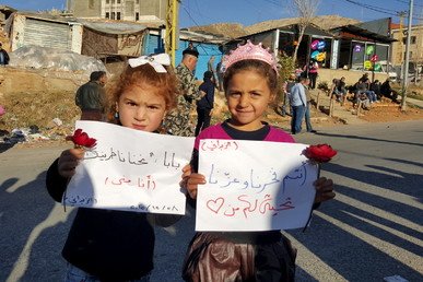 فتيات يحملن لافتات أثناء انتظارهن عند المعبر الحدودي بين لبنان وسوريا لوصول أقاربهن من المقاتلين المتمردين الذين غادروا بلدة الزبداني، 28 ديسمبر/كانون الأول 2015. 