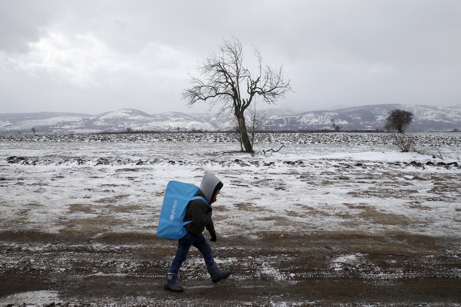 طفل مهاجر يمشي في حقل مكسو بالثلج بعد عبورهم الحدود المقدونية