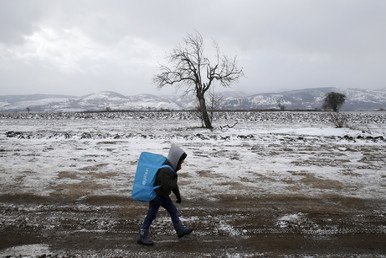 طفل مهاجر يمشي في حقل مكسو بالثلج بعد عبورهم الحدود المقدونية