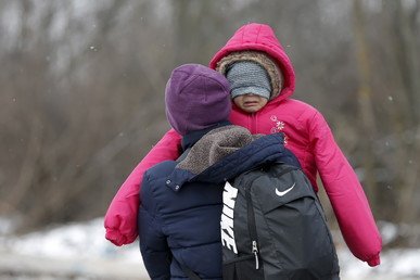 مهاجر يحمل طفله وهو يمشي في حقل مكسو بالثلج بعد عبور الحدود المقدونية