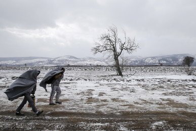 مهاجران يمشيان في حقل مكسو بالثلج بعد عبورهما الحدود المقدونية