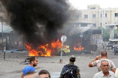 عسكري سوري وعدد من المدنيين يفحصون مكانا في طرطوس تعرض للقصف