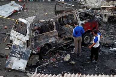 شخصان يفحصان سيارة مدمرة نتيجة للقصف