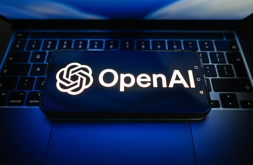 شعار شركة "OpenAI" معروضة على هاتف ذكي موضوع فوق جهاز كمبيوتر محمول