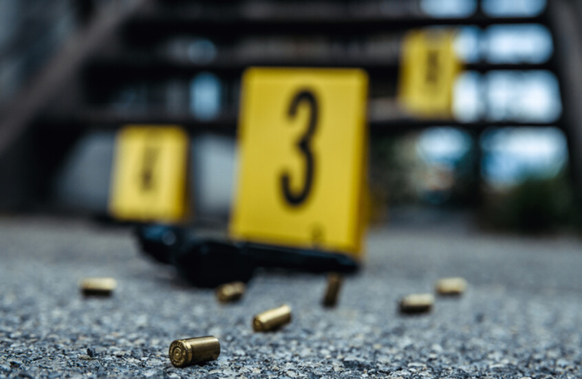 فوارغ لطلقات نارية معدنية ذهبية اللون في مقدمة الصورة وخلفيتها فوق أرضية خرسانية، وتظهر ثلاث لافتات بلاستيكية صفراء اللون تستخدم عادة من قبل محققي الشرطة لترقيم الأدلة