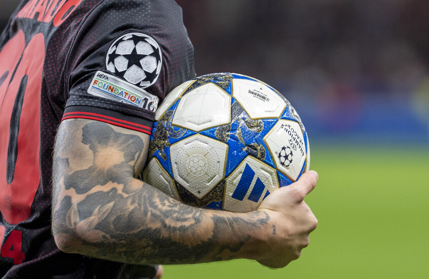 أليخاندرو غريمالدو لاعب باير ليفركوزن حاملا كرة "أديداس" الخاصة بدوري أبطال أوروبا يظهر على كم القميص شعار دوري أبطال أوروبا وشعار مؤسسة الاتحاد الأوروبي لكرة القدم "يويفا"
